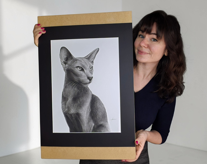 Karina Kraus hält ein handgefertigte Tierportraits einer Orientalischkurzhaar Katze. Schwarz-weiß mit Passepartout